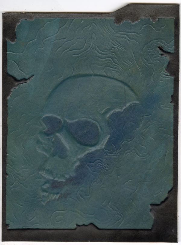 Woodcut embossed on leather showing topographical ridges with a skull face rising from the center